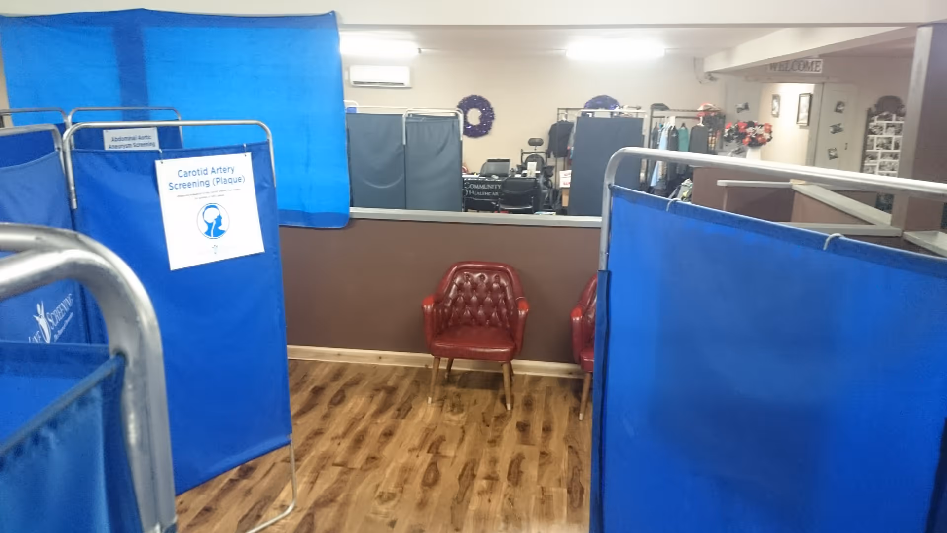 Blue partitioned cubicles inside a senior care facility, with a carotid screening sign and red chairs.