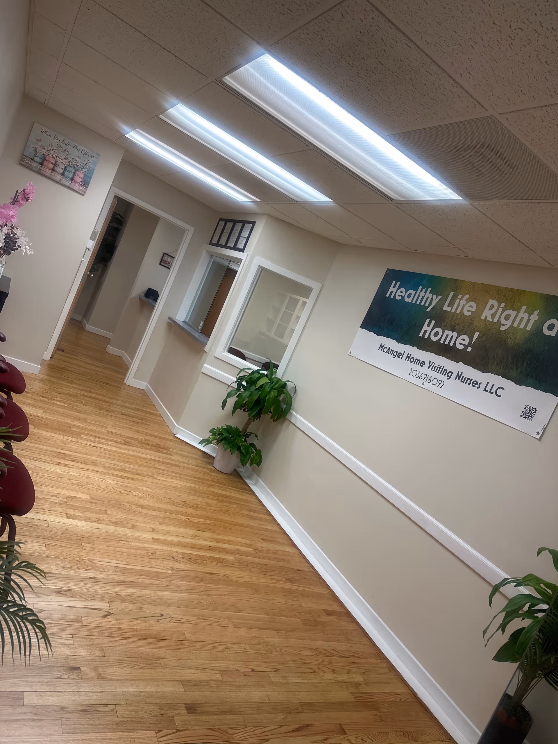 Interior hallway of a senior care facility with plants and a reception window.