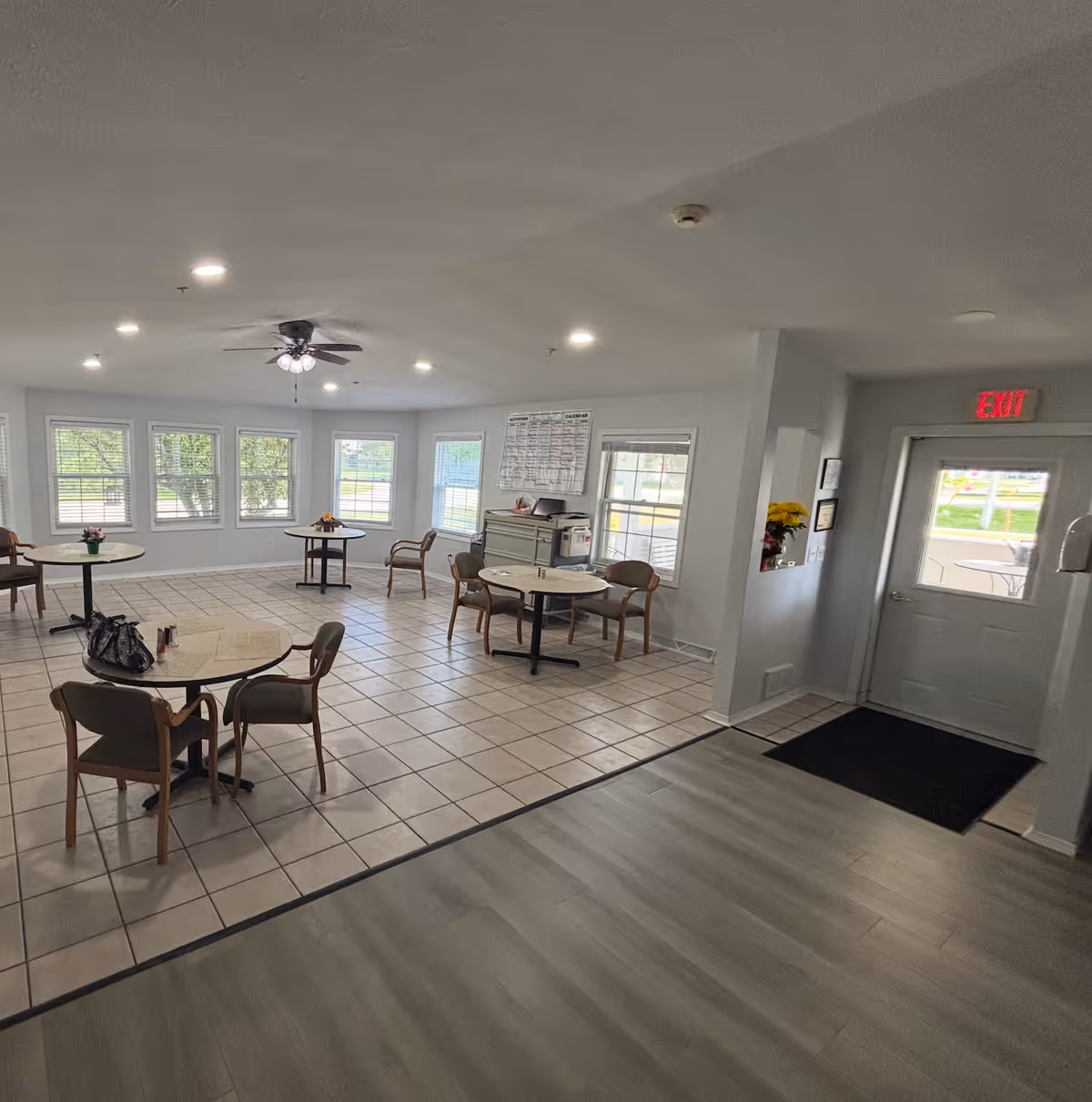 Bright dining area in a senior living facility with round tables and windows.