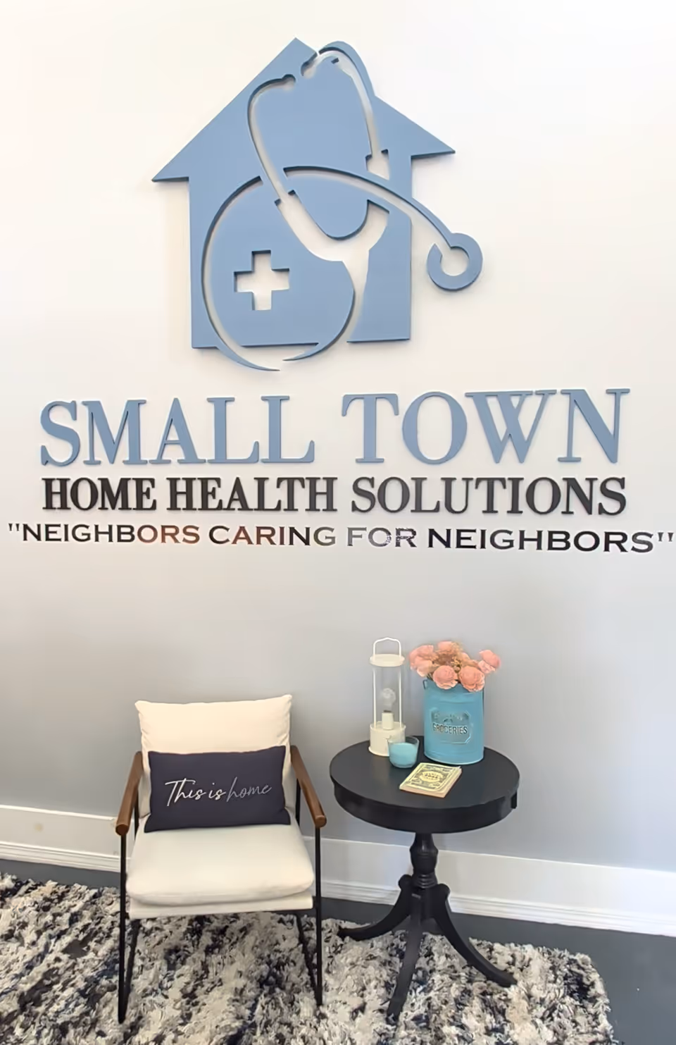 Interior lobby with a large Small Town Home Health Solutions sign, chair, and decorative table.