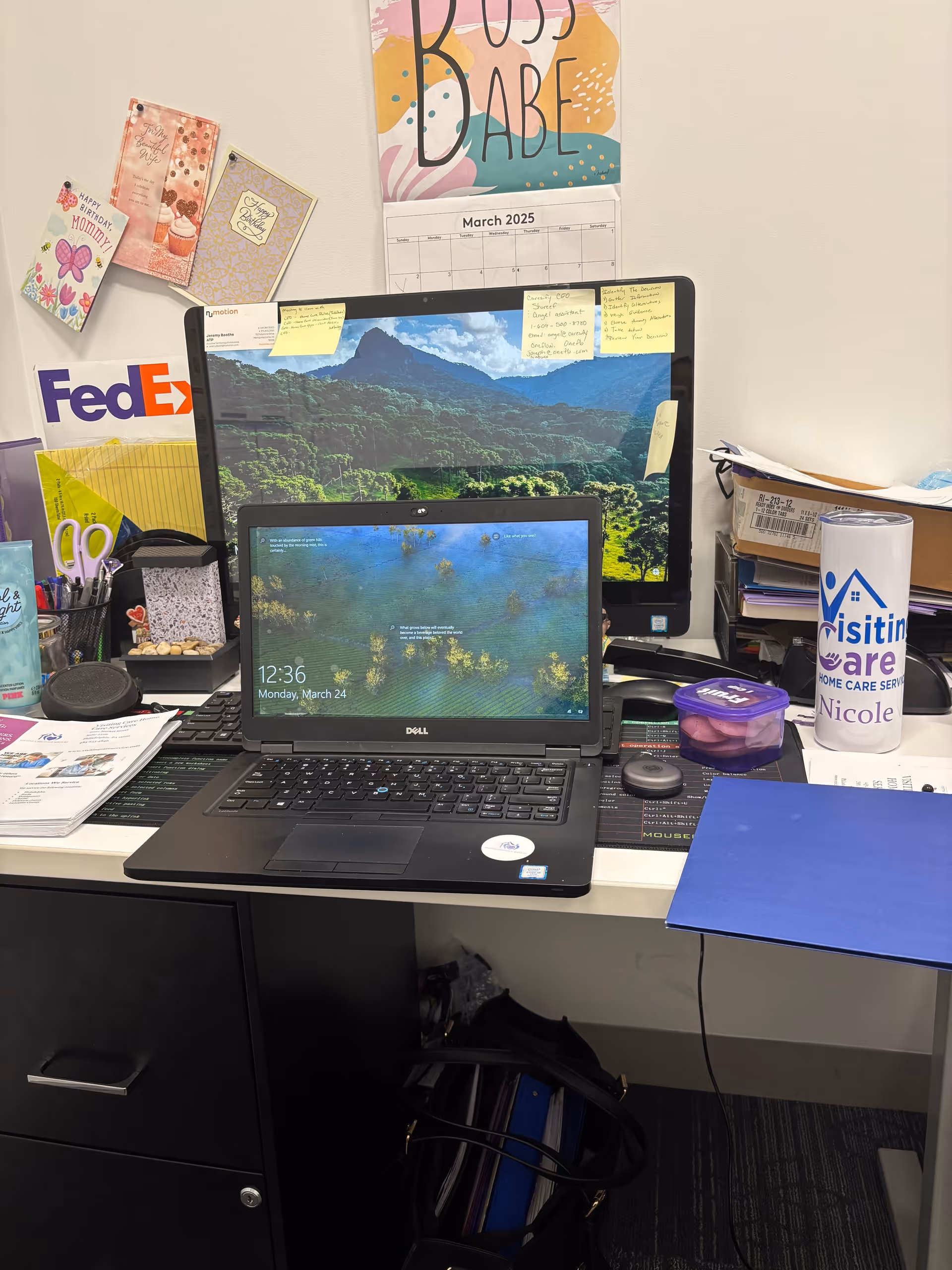 Office desk with laptop, monitor showing a landscape, and organized paperwork in a care home office.