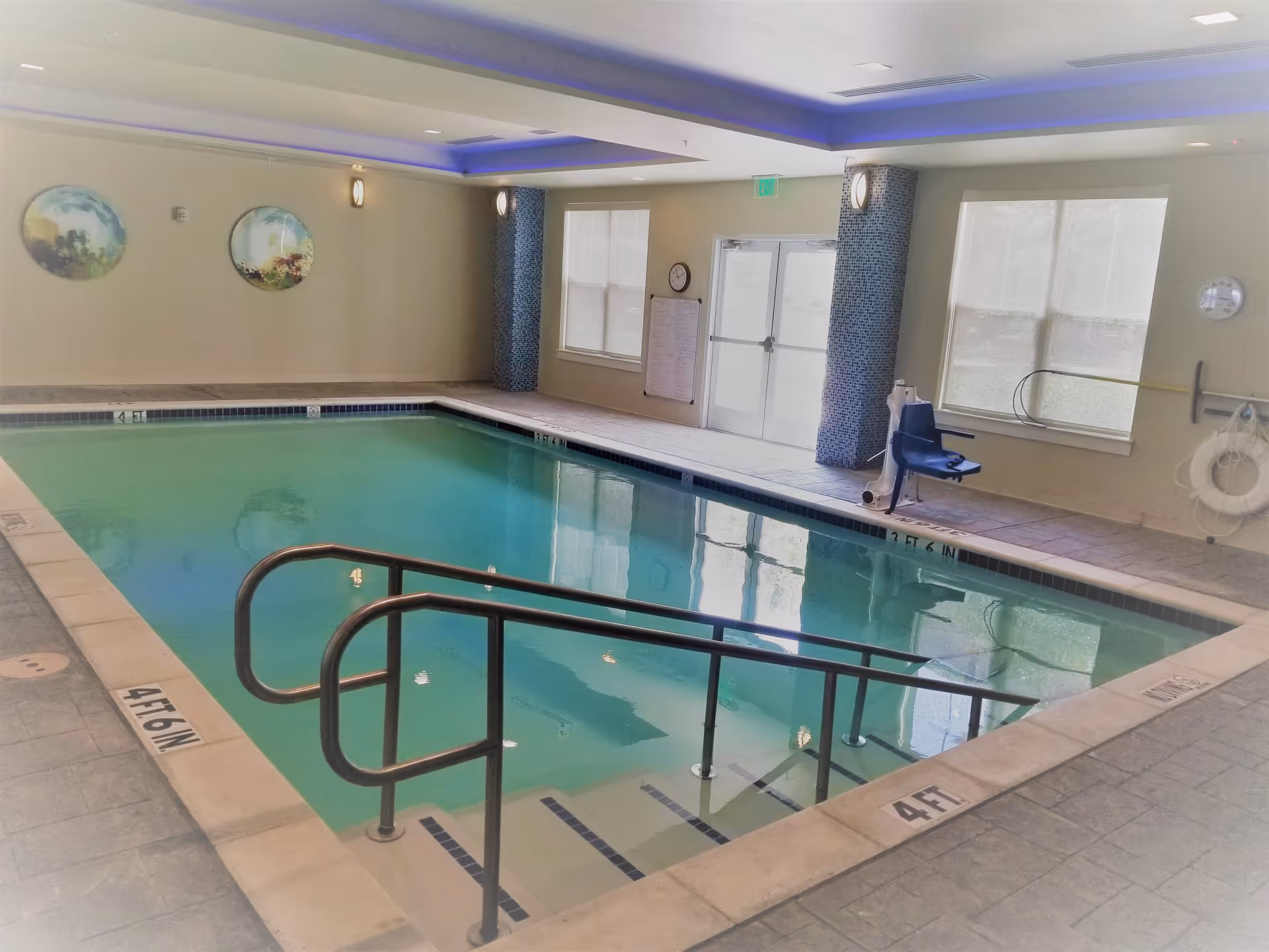 Indoor pool at a senior living center with safety rails and blue mosaic columns.