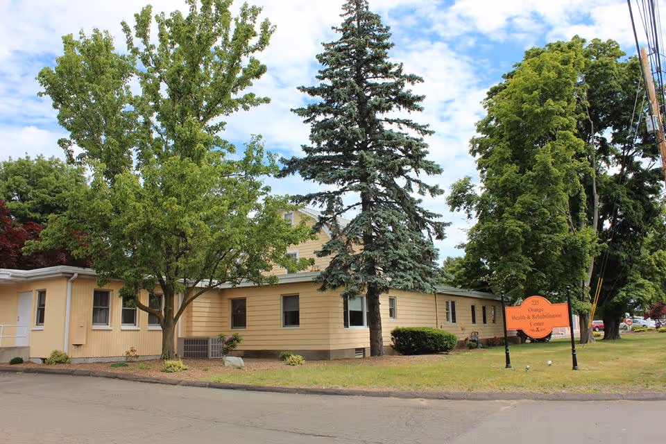 Exterior view of Orange Health Care Center, a beige senior facility, with trees and a sign.