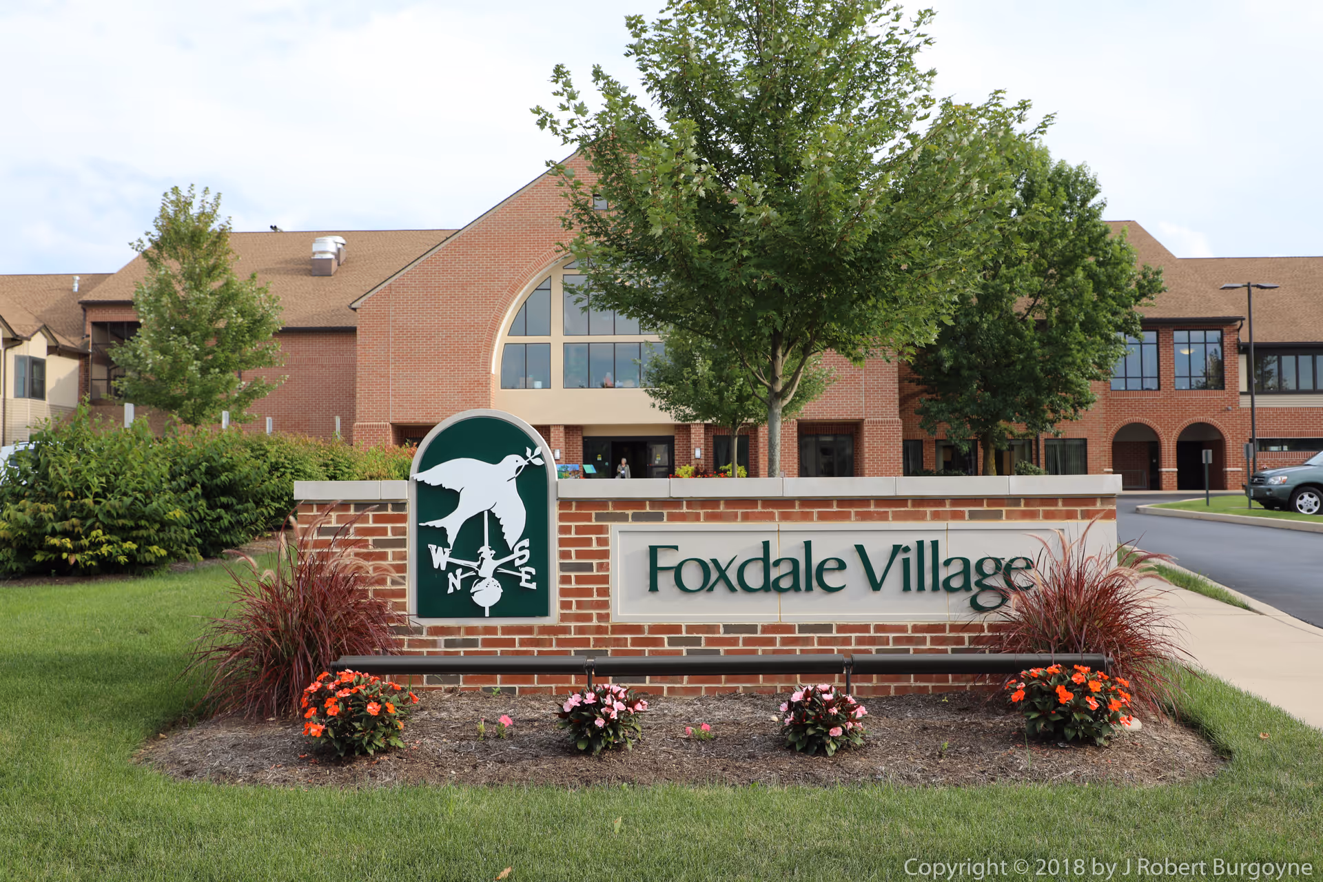 Exterior view of Foxdale Village with brick building, trees, and a sign in a landscaped lawn.