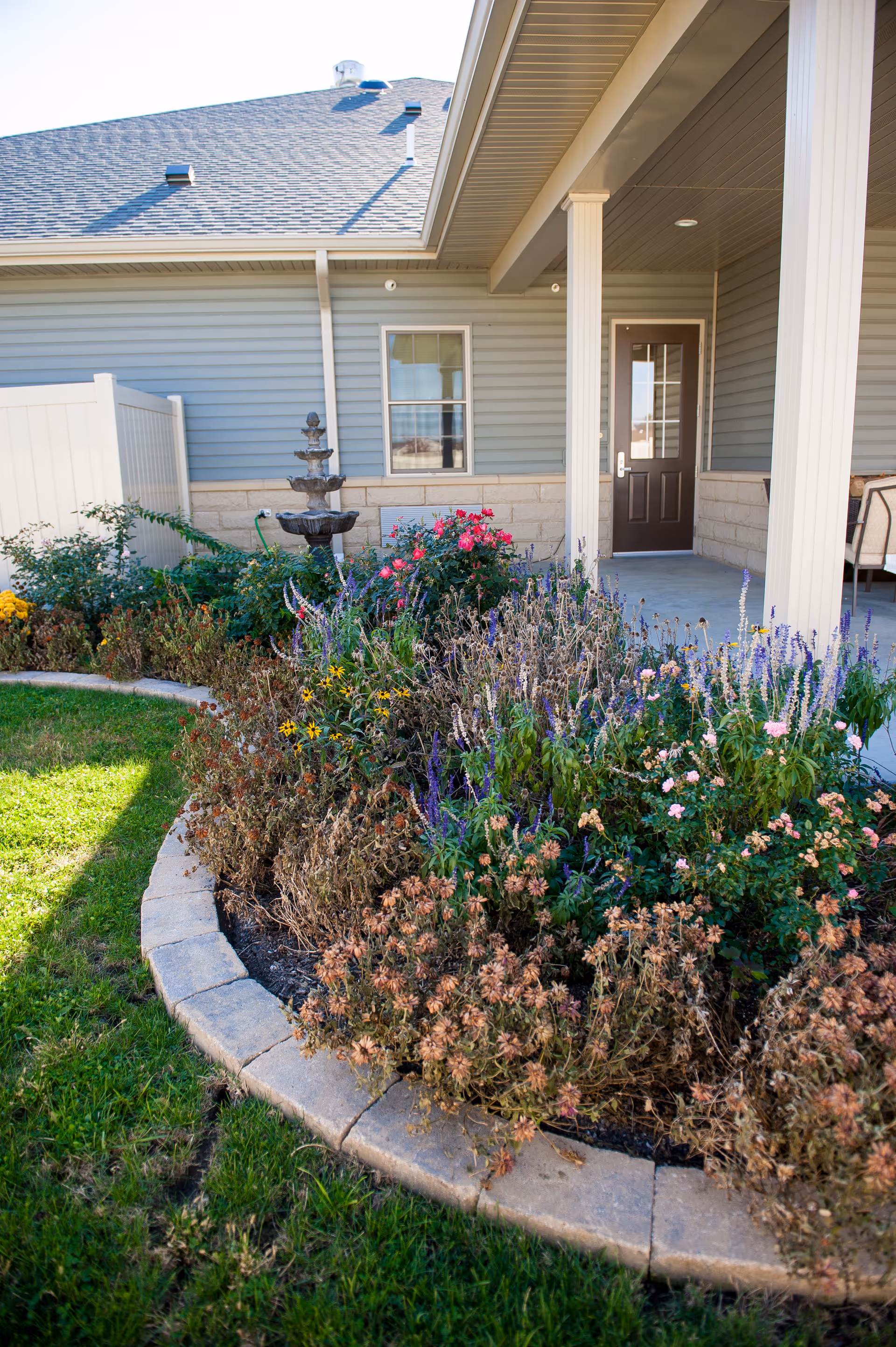 Front entrance of a blue residence with a landscaped flower bed and fountain.