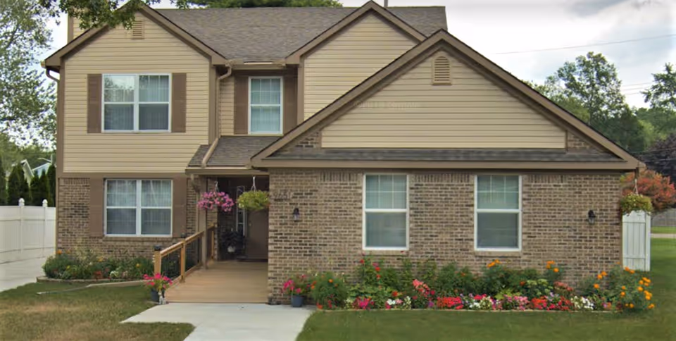 A two-story brick and siding senior care building with a flower-filled front yard.
