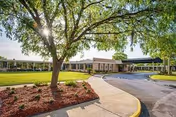 Exterior view of a senior living facility with a curved driveway, trees, and lawn.