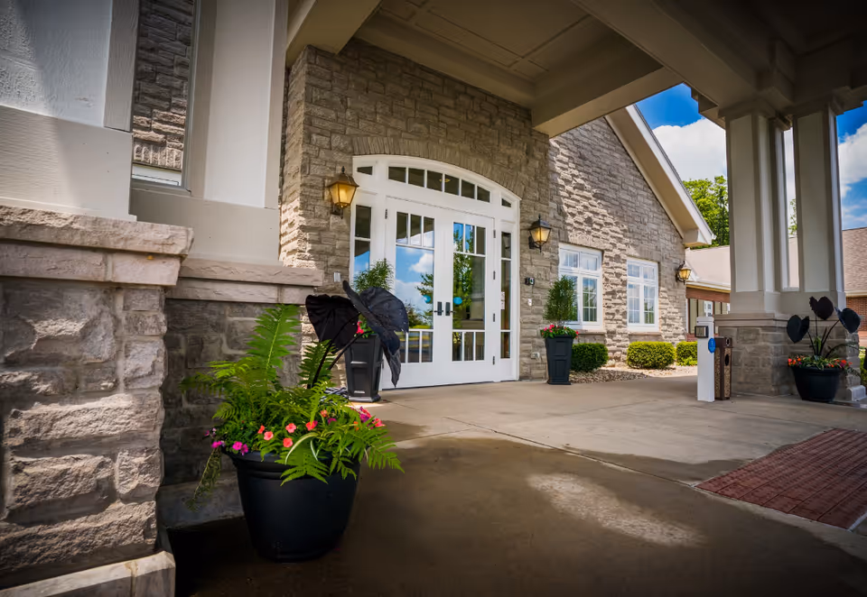 Stone exterior entrance of The Inn at Ashland Woods with glass doors and potted plants.