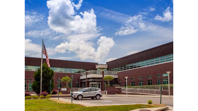 Brick senior living facility exterior with entrance, flagpole, and parked car in front