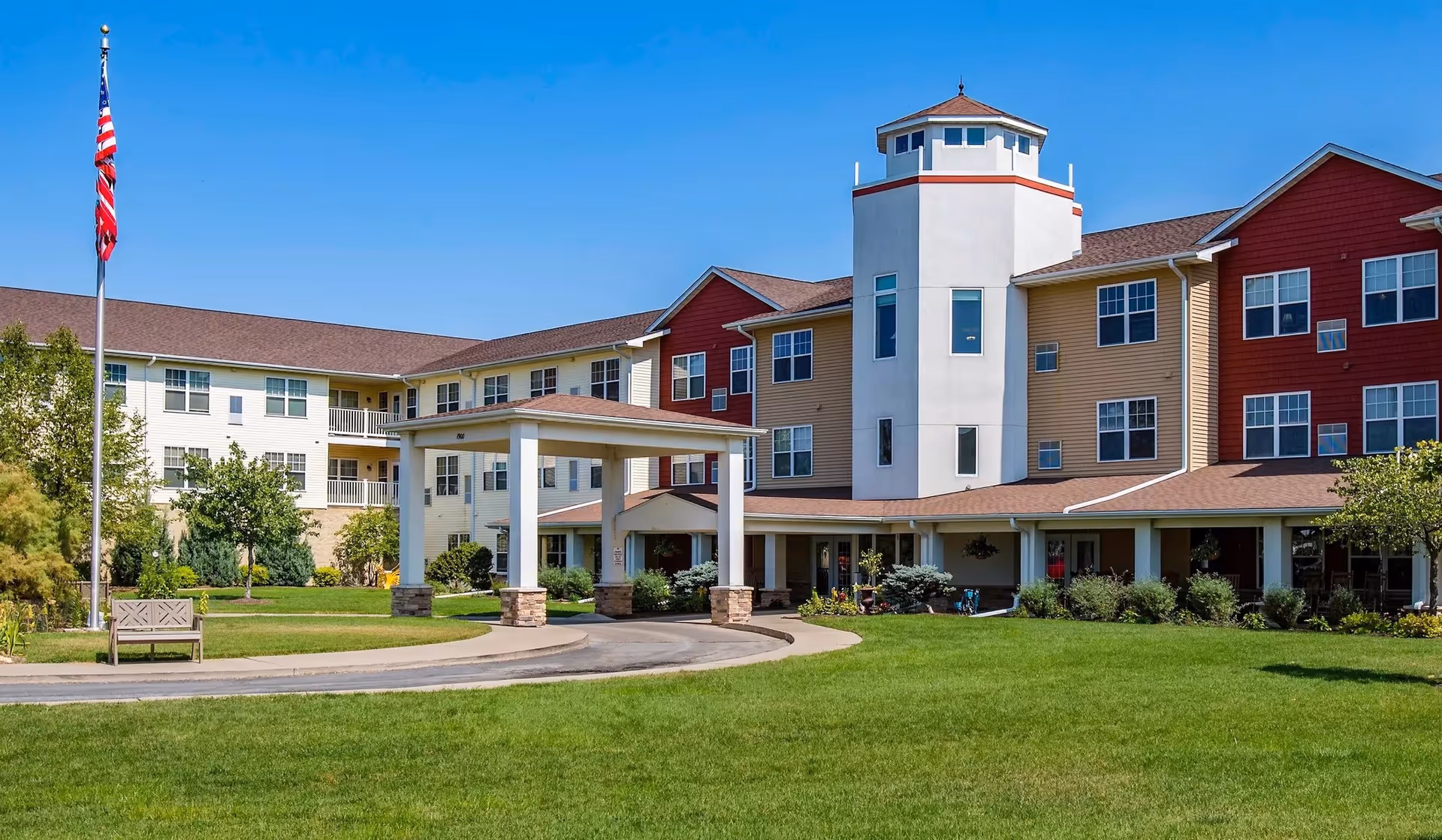 Exterior view of a multi-colored senior living campus with a tower, lawn, and flagpole.