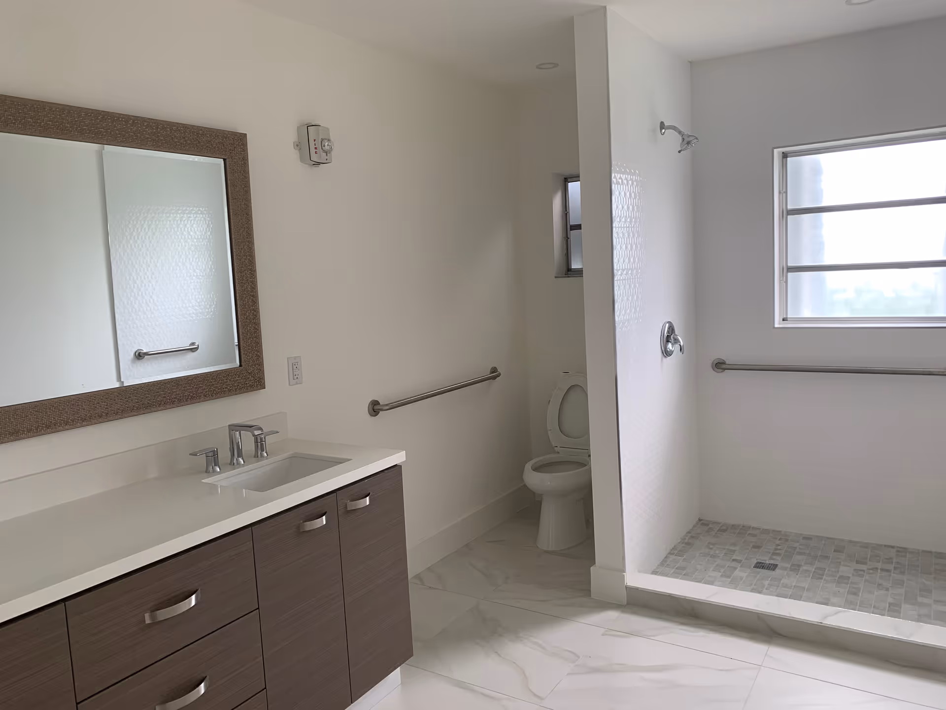Modern bathroom with sink, mirror, toilet, and accessible shower in a senior living facility.