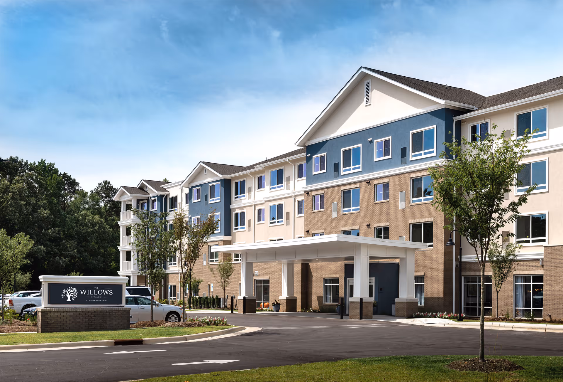Exterior view of a multi-story senior living facility with a covered entrance and parking.