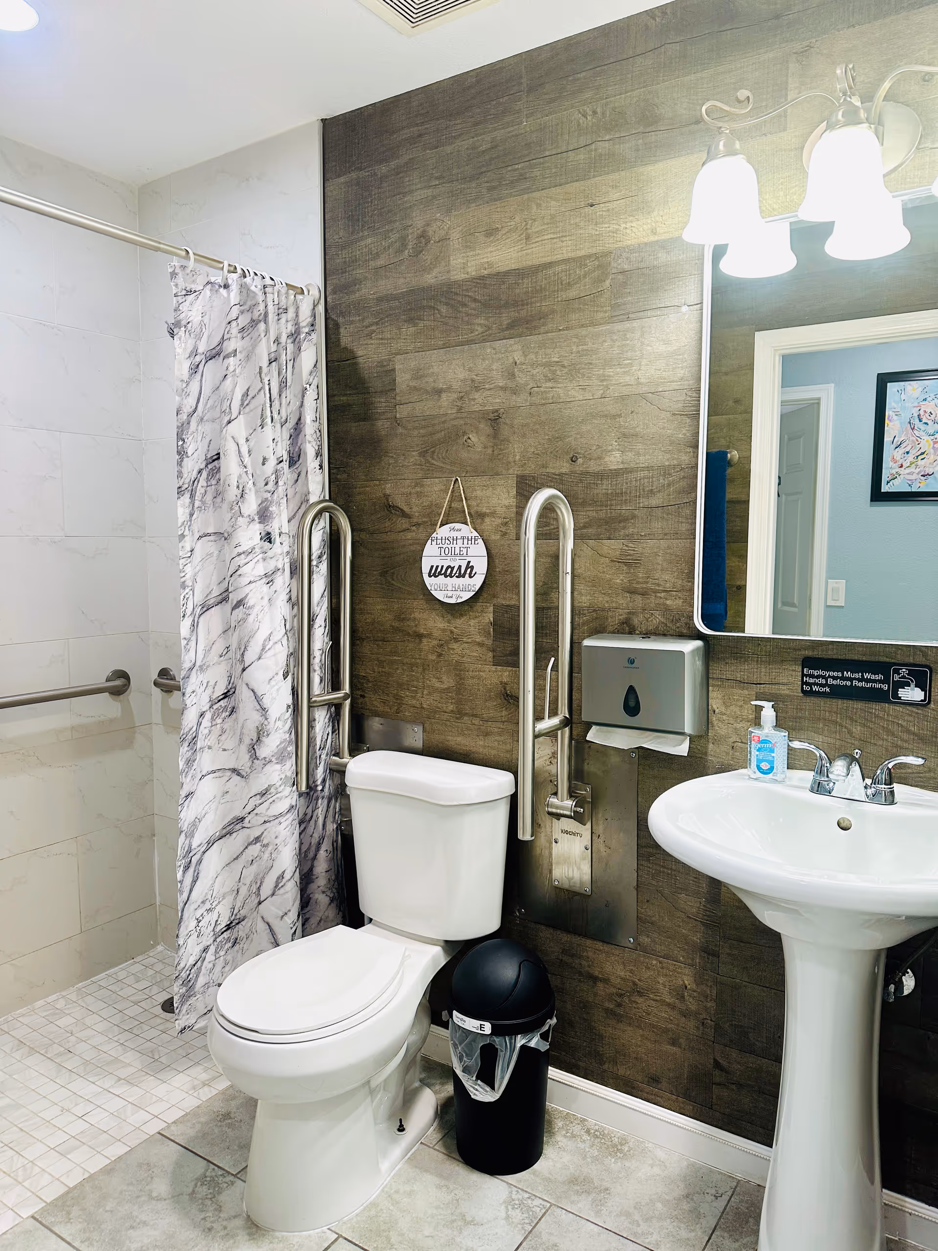 Accessible bathroom with toilet, pedestal sink, shower curtain, and grab bars.