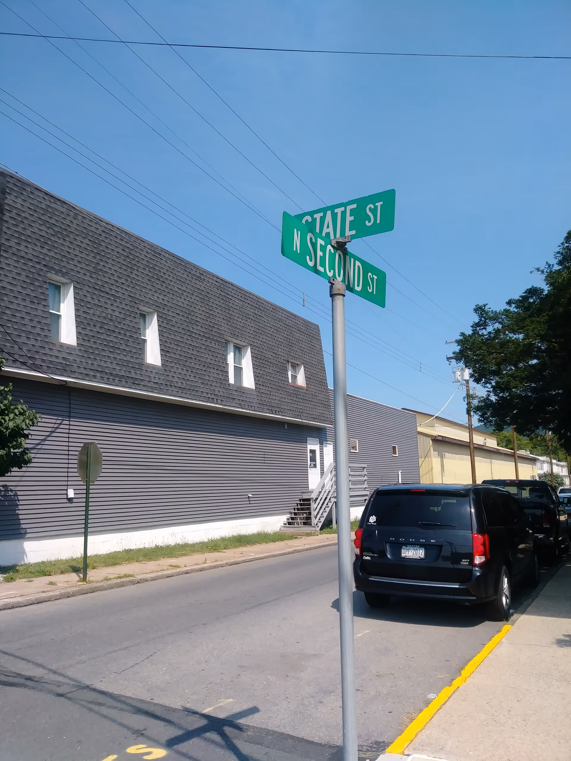 Street corner view of a gray metal-sided building with parked cars and green street signs.