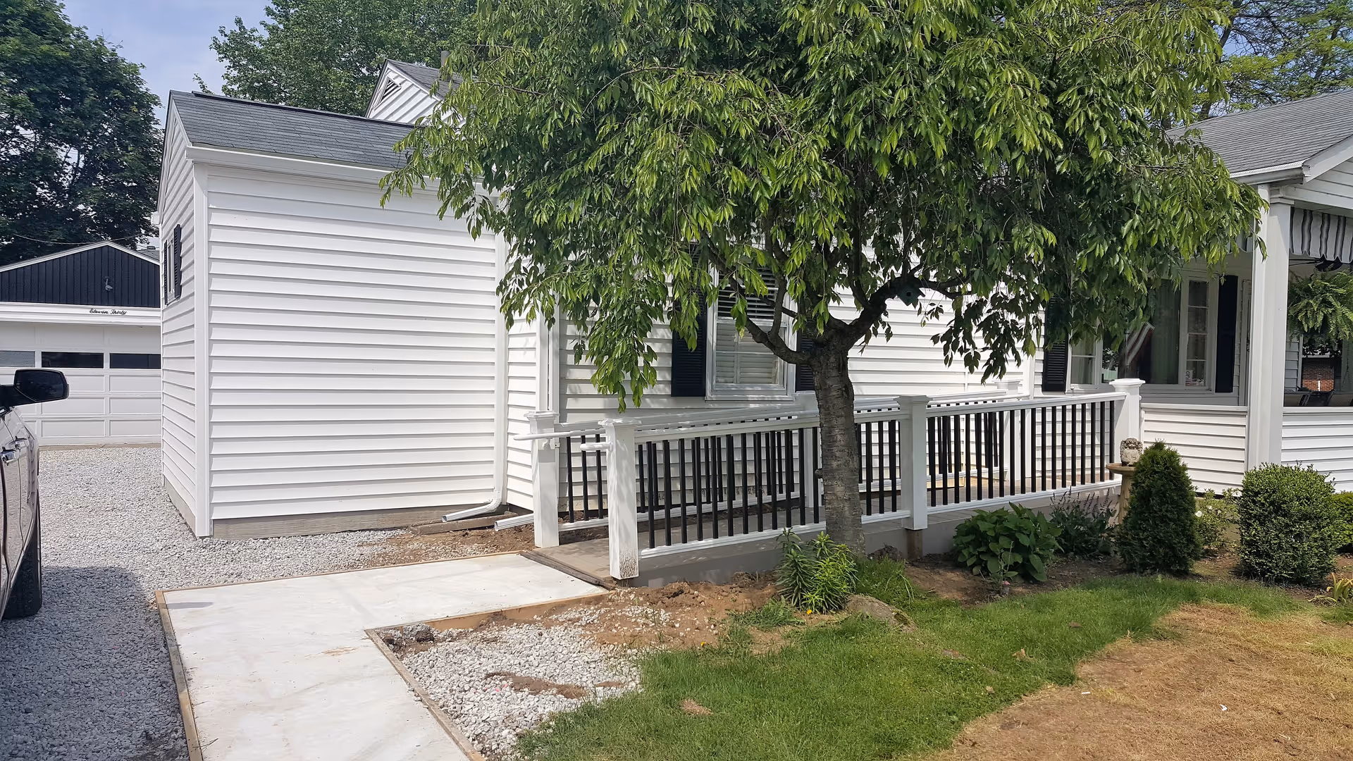 White single-story senior living facility exterior with ramp, railing, and a leafy tree.