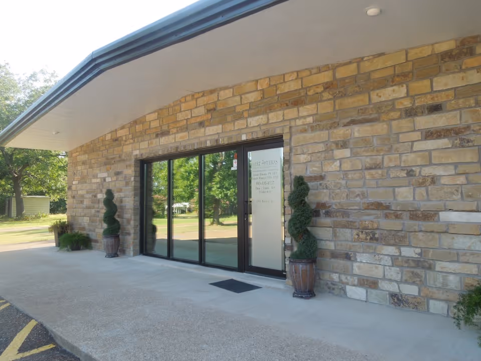 Stone exterior with glass entrance doors, curved awning, and potted topiary near East Texas Physical Therapy.