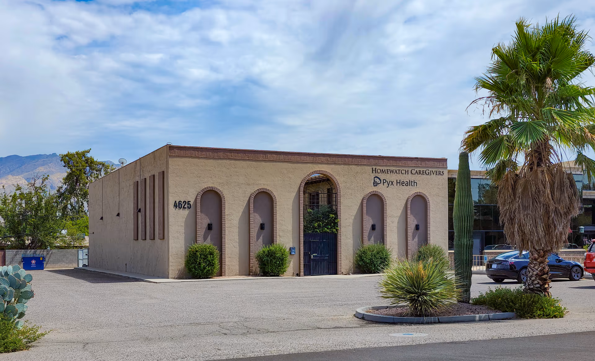Exterior view of a beige building with arched entrances, palm trees, and desert landscaping.