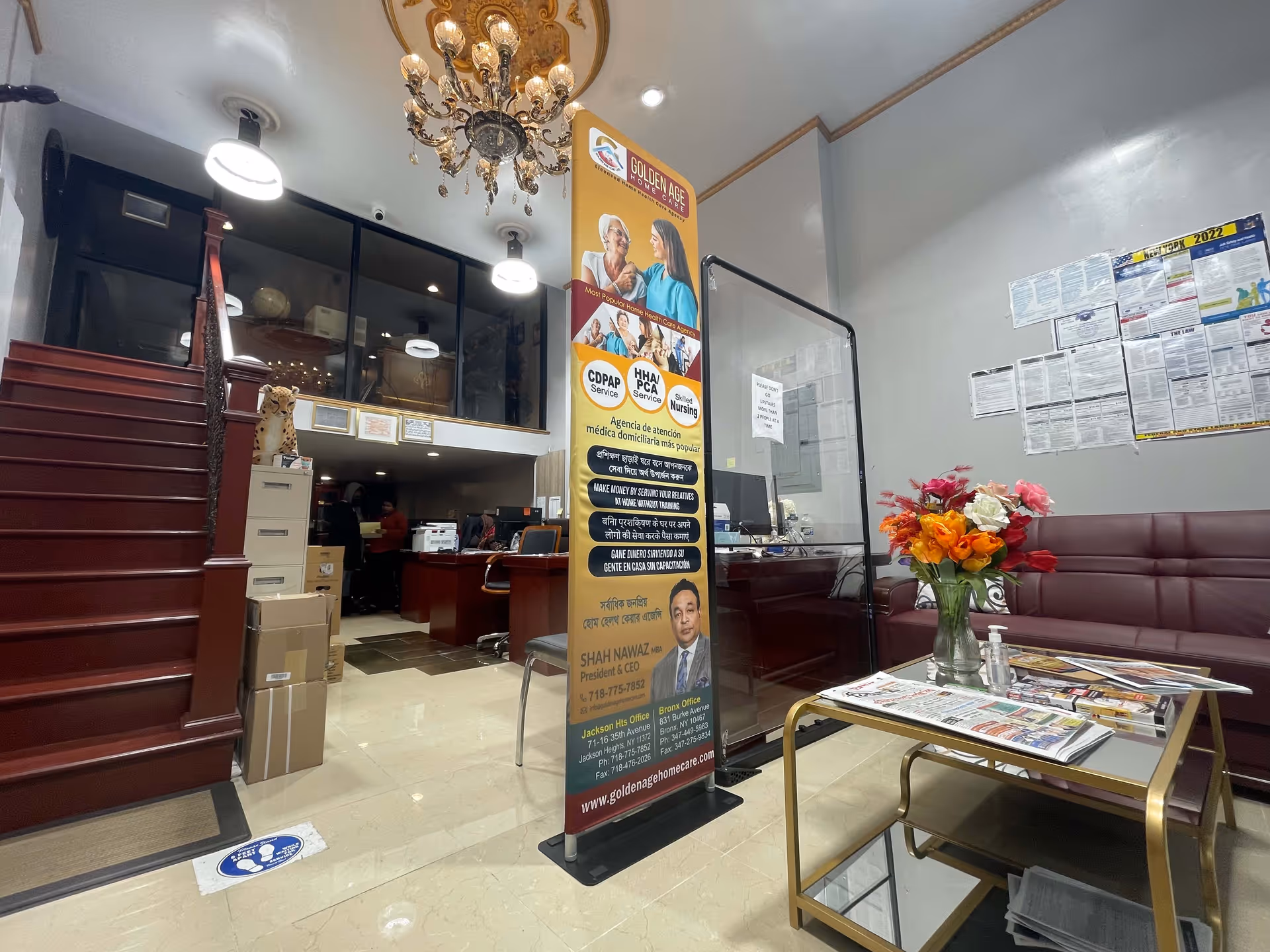 Interior lobby of Golden Age Home Care with staircase, banner, reception desk, seating, and flowers.