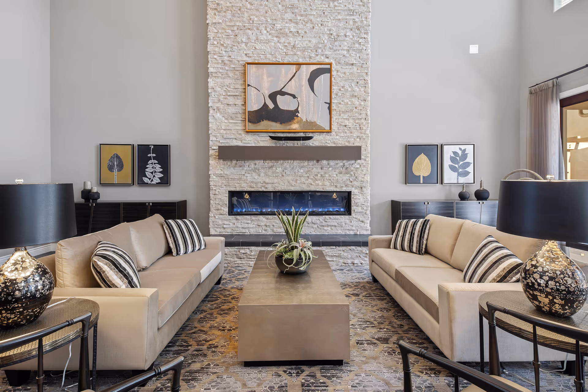 Two beige sofas face a central stone fireplace with artwork, coffee table, and lamps.