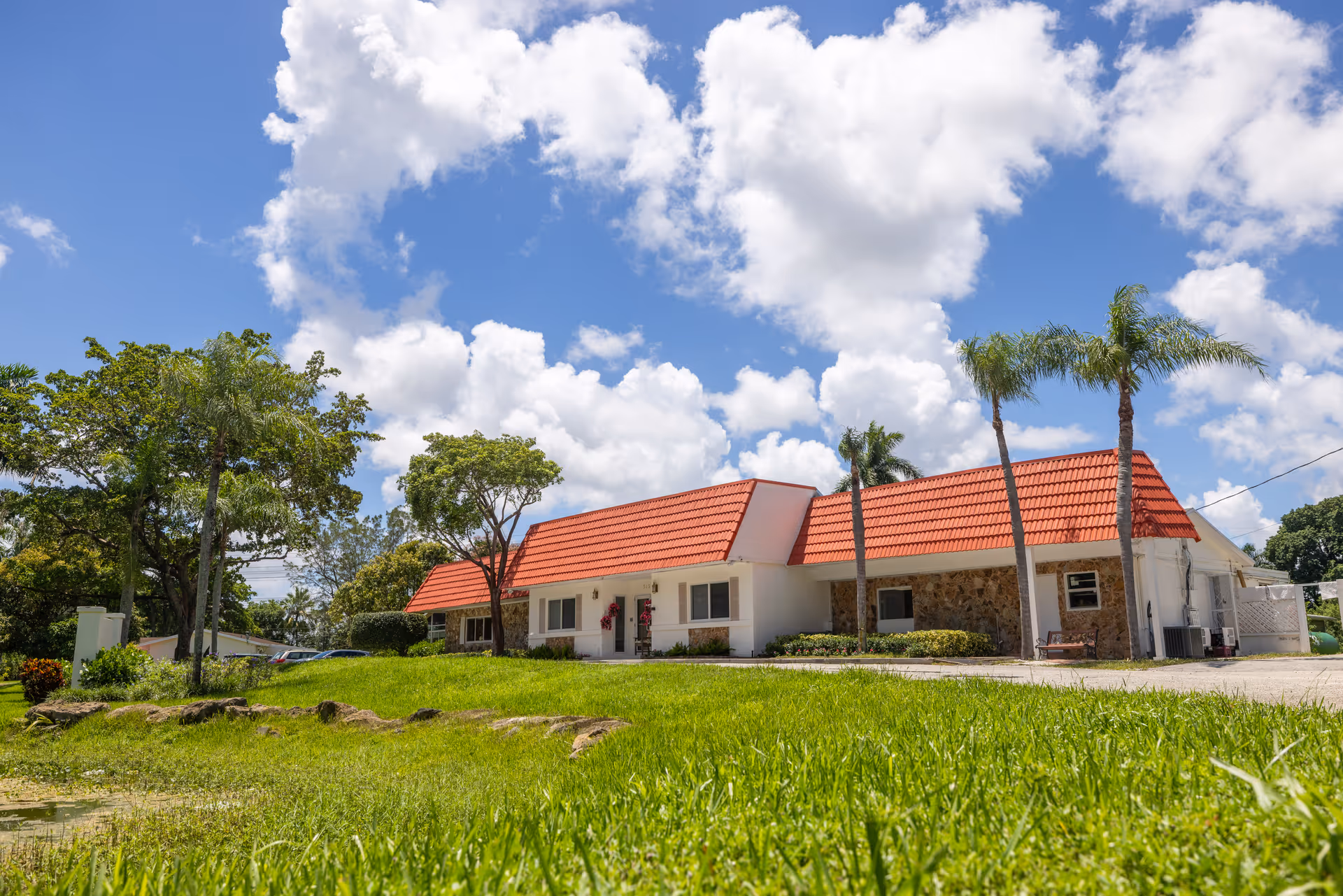 Single-story building with red-tiled roof, palm trees, and a green grassy front yard.