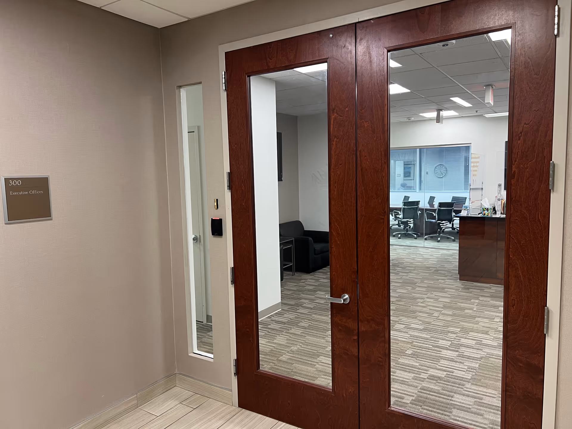 Wood-framed glass double doors open to a conference room with chairs and a reception desk.
