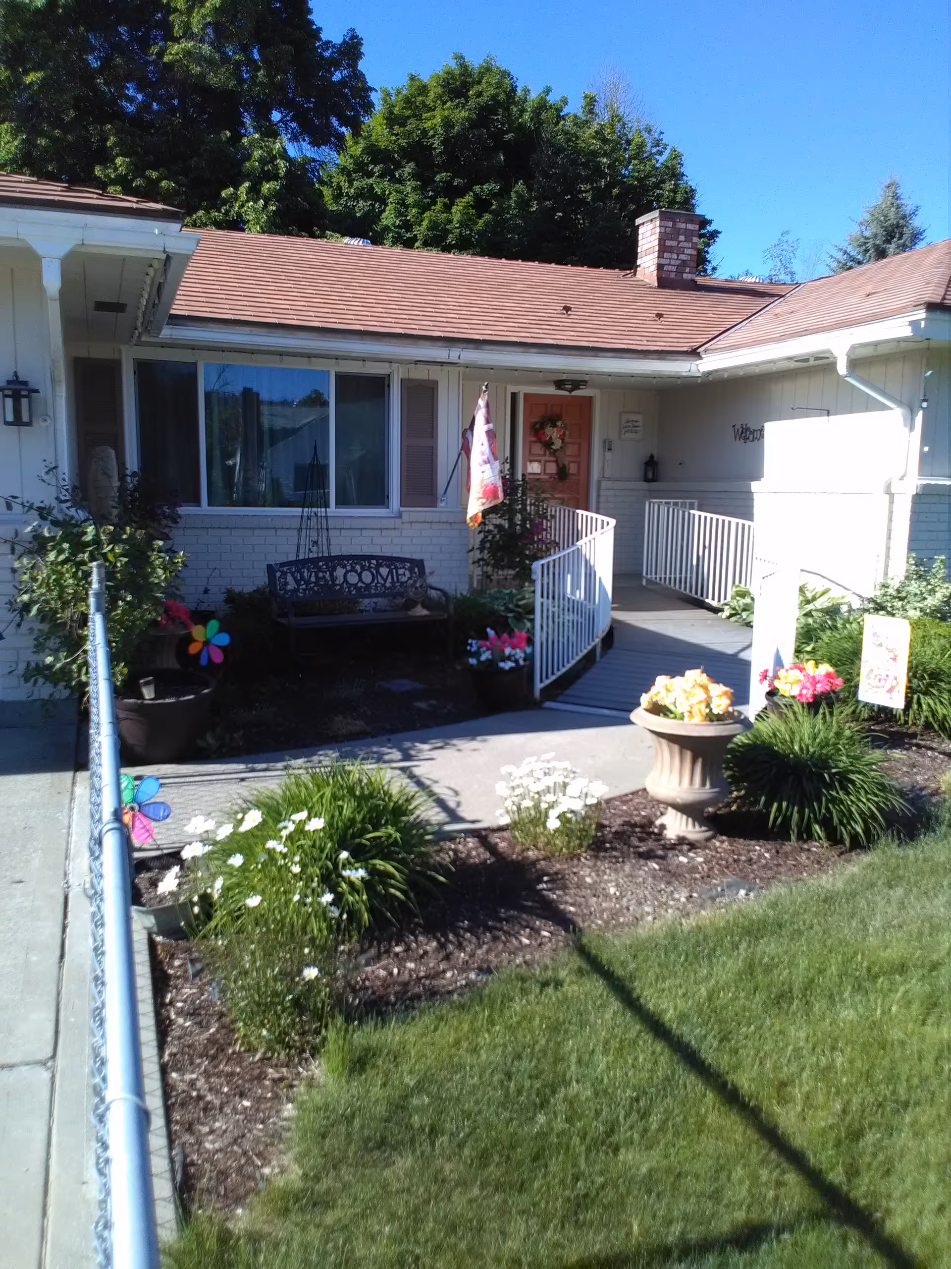 Front exterior of a single-story house with a porch, garden, and potted flowers.