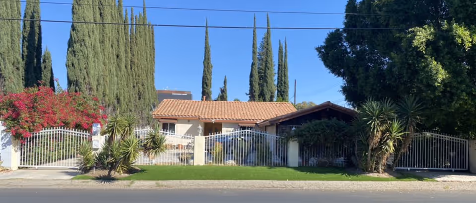 Front exterior of Tarzana Senior Living Inc, gated yard with palm trees.