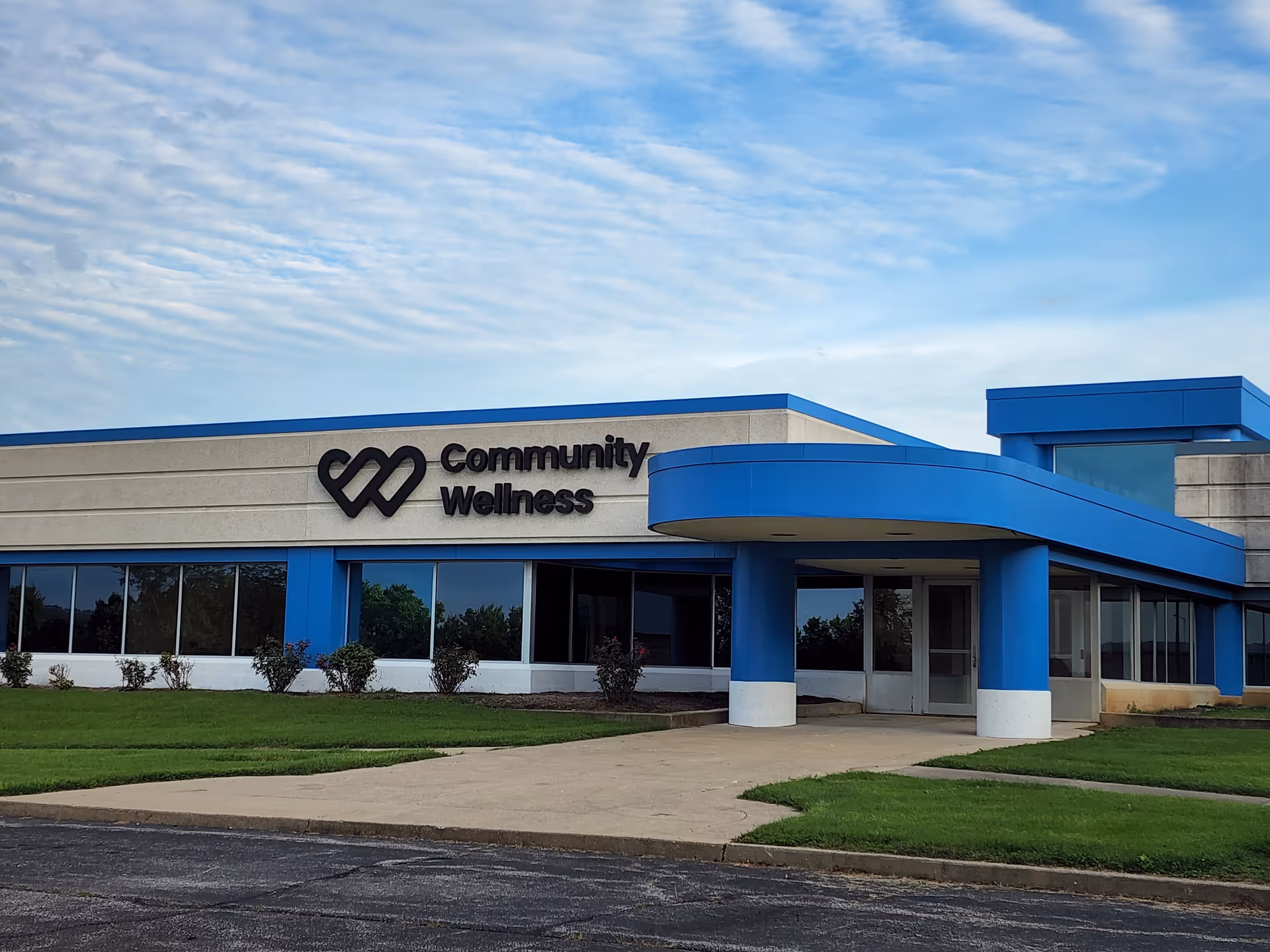 Exterior view of a blue-trimmed building labeled Community Wellness, with entrance canopy and landscaping.