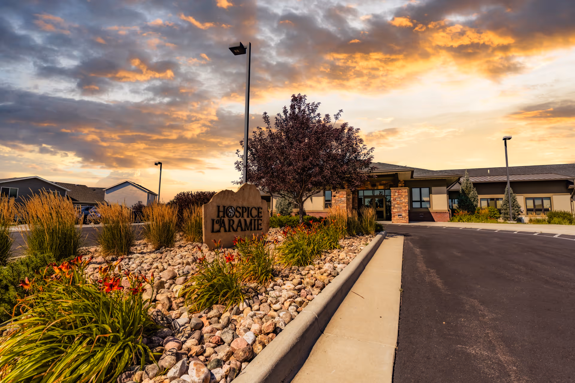 Stone sign reading Hospice of Laramie at the building entrance, surrounded by rocks and plants.