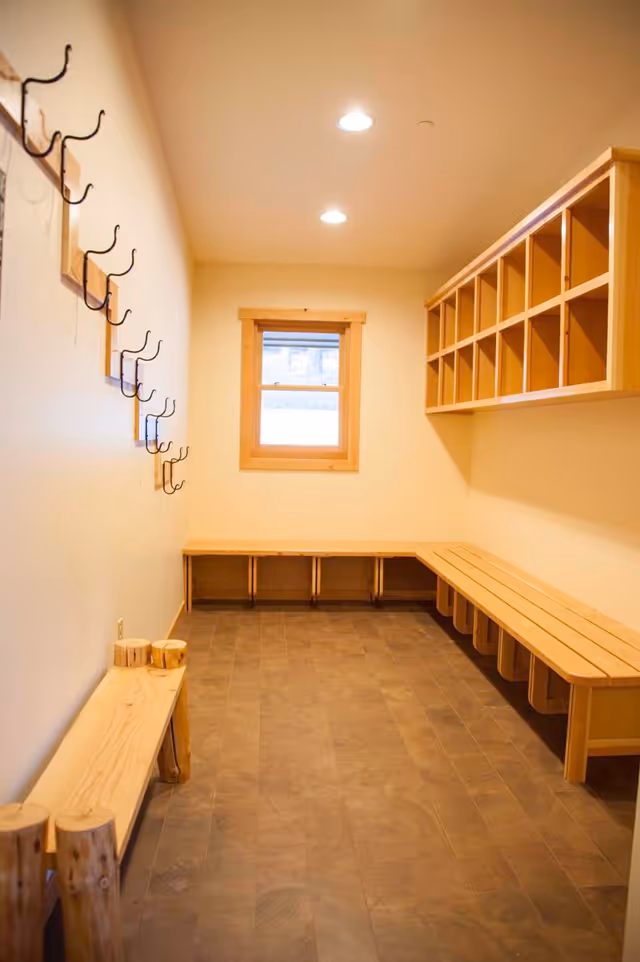 A well-lit interior mudroom with long wooden benches, hooks, and cubbies.