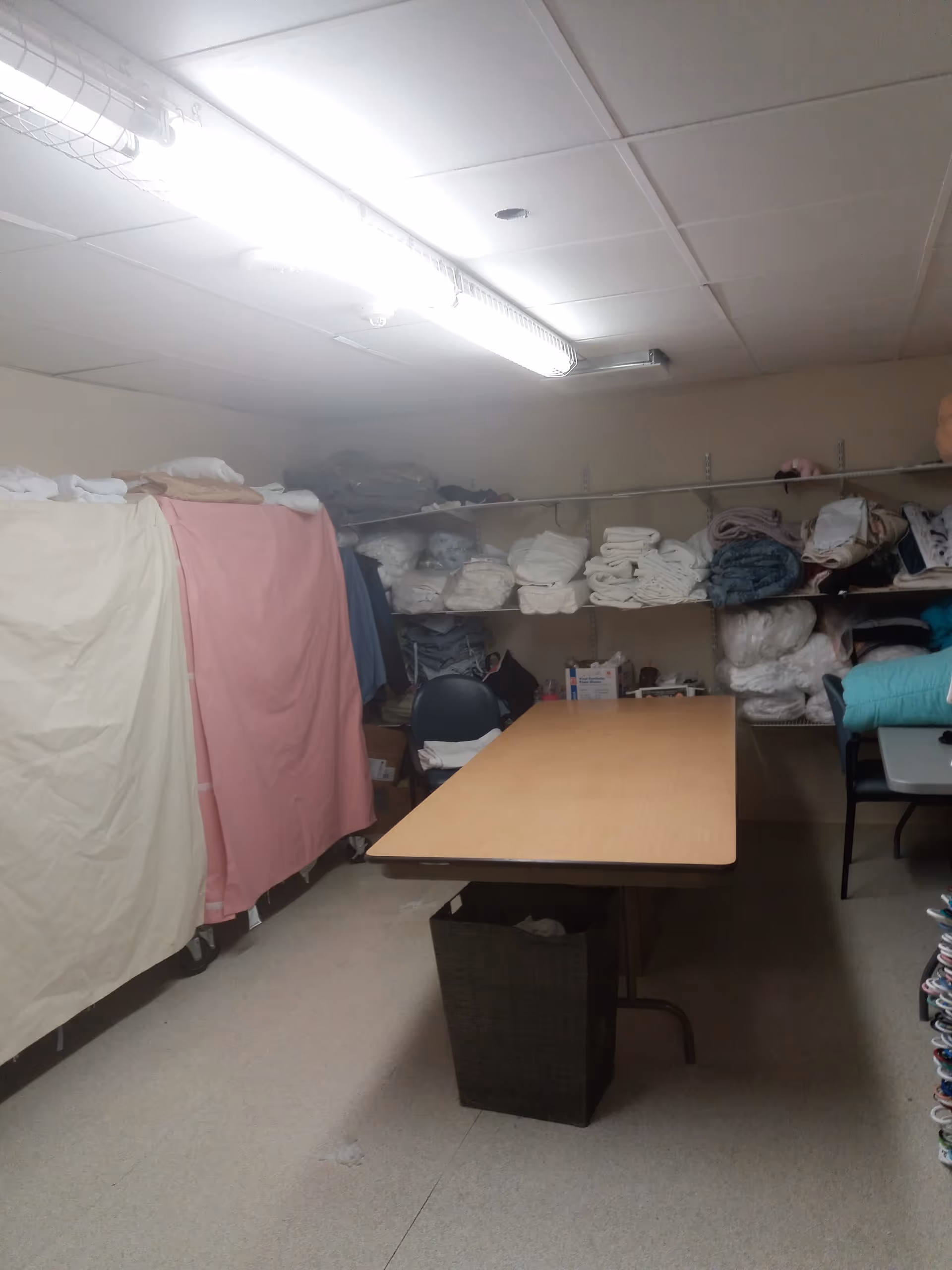 Utility room with shelves of folded linens, blankets, and a central wooden table.