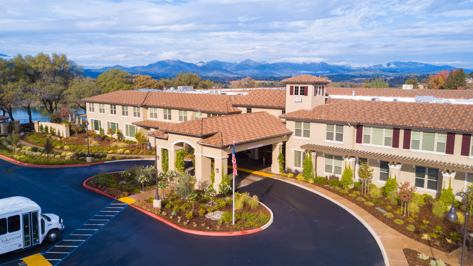 A multi wing senior living facility with red tiled roof, circular driveway, and mountains in background.