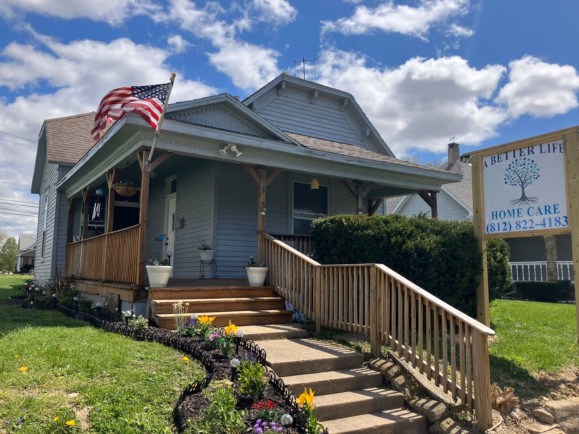 Small gray house-style building with a porch, American flag, and Better Life Home Care sign.