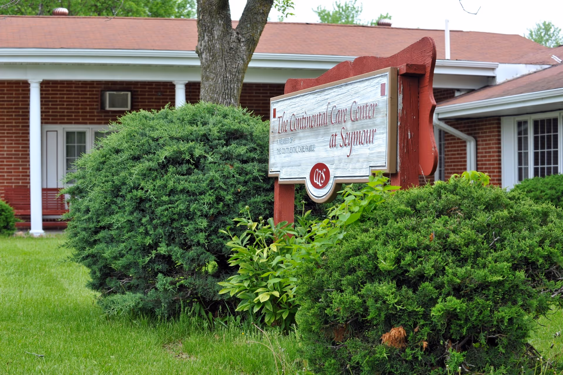 Front exterior of Continental Care Center with sign, brick building, columns, and greenery.