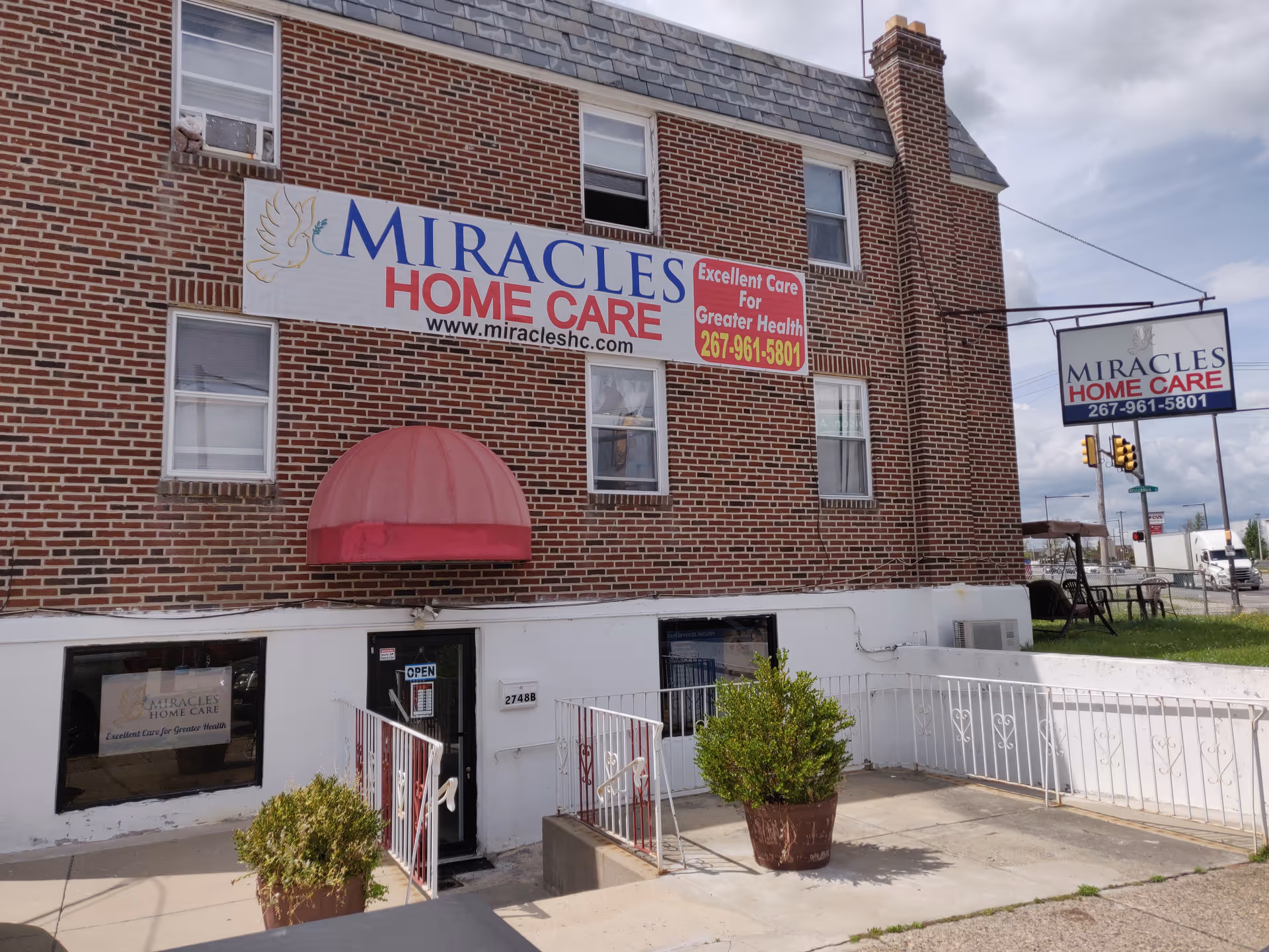 Brick building exterior with Miracles Home Care sign, pink awning, and entry doors.