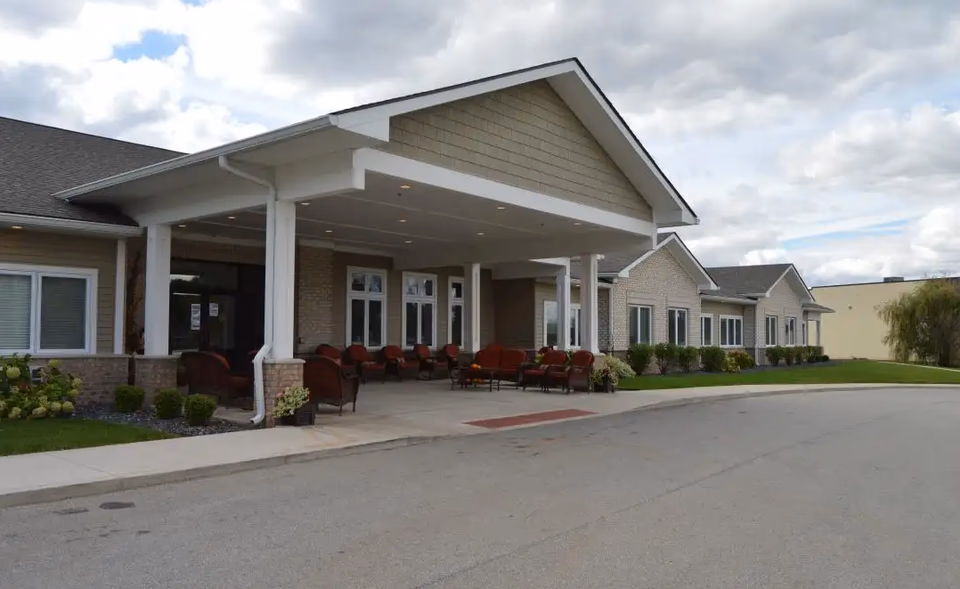 Exterior of a senior living facility with a covered entrance and red outdoor seating.