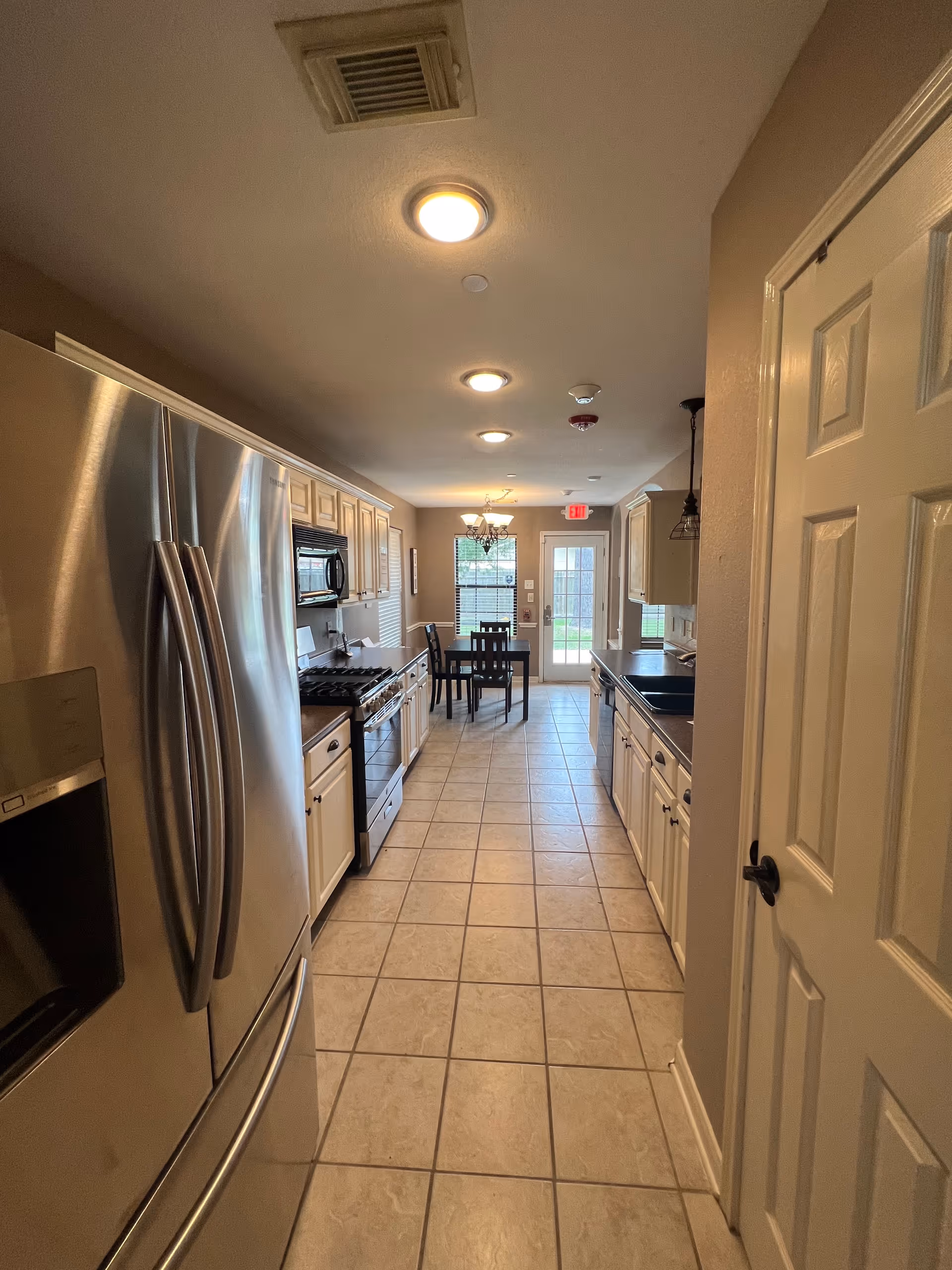 Long kitchen with stainless appliances, white cabinets, and a dining table at the far end.