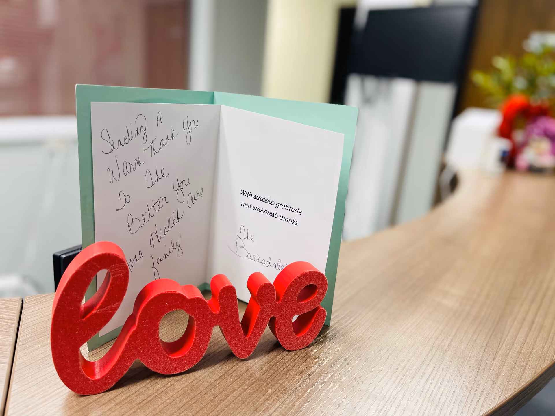 Close-up greeting card and red love decor on a wooden desk in a bright reception area.