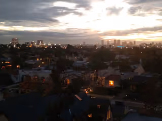 Sunset over a city skyline with residential rooftops and trees in foreground.