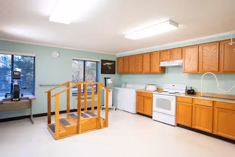 Senior living facility kitchen with cabinets, stove, washer and dryer, and a small wooden platform.