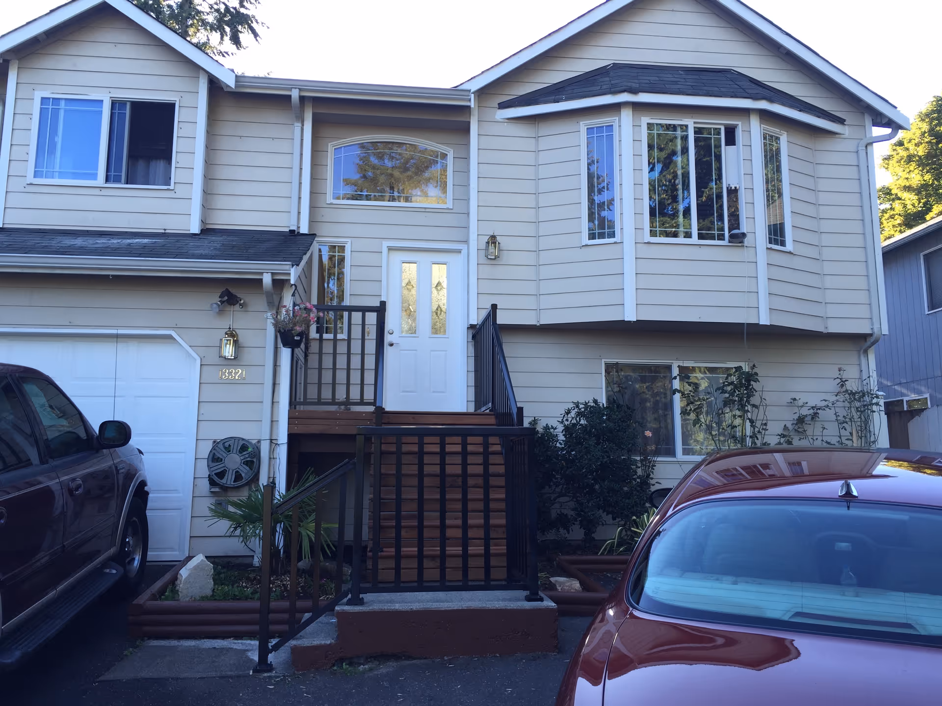 Two-story beige residence with a front staircase, porch, and parked cars.