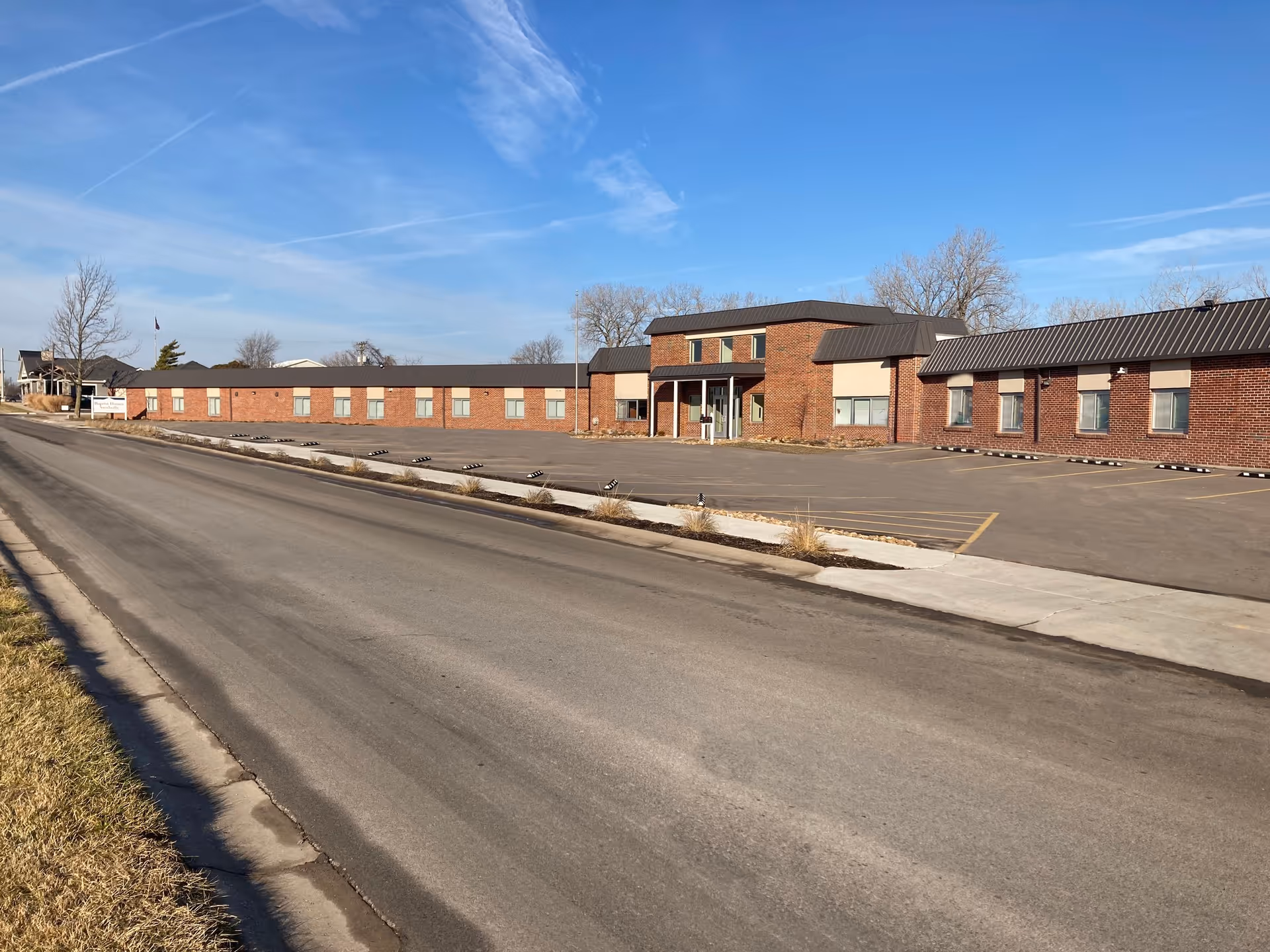 Brick senior living facility exterior with a long one-story building and a paved parking lot.