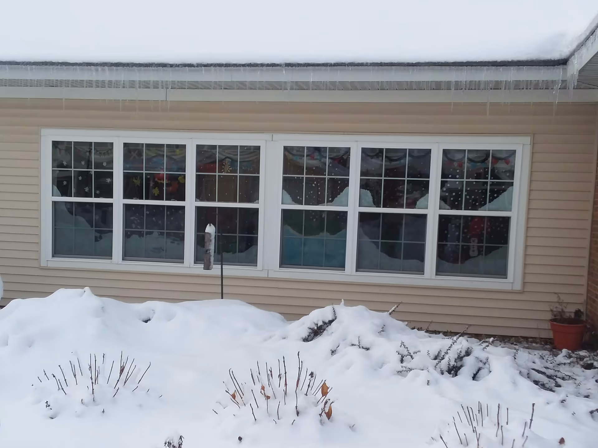 Snow covers the ground outside a beige senior living facility with large windows.
