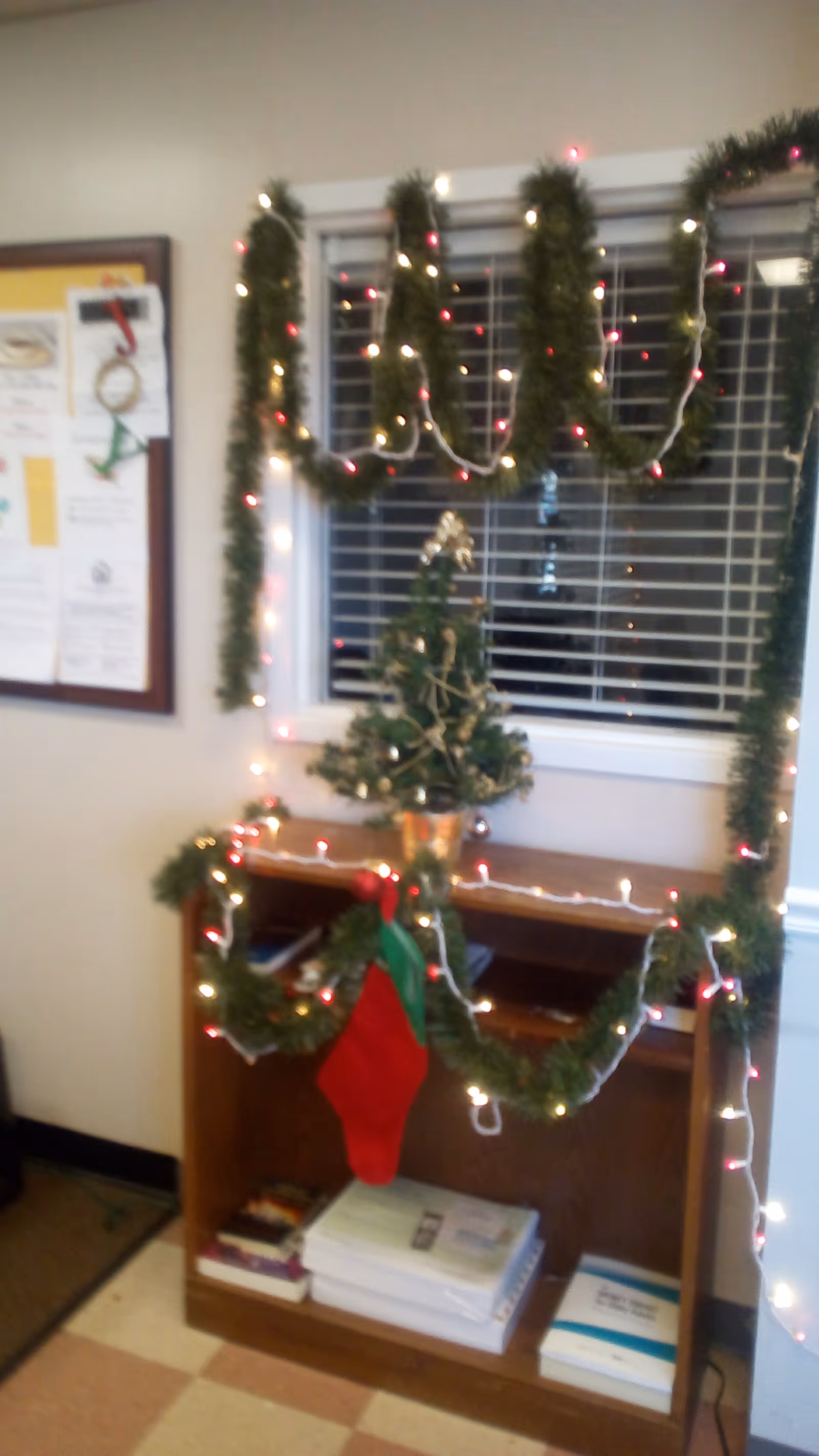 Festively decorated interior corner with garlands, lights, a small Christmas tree, and a shelf.