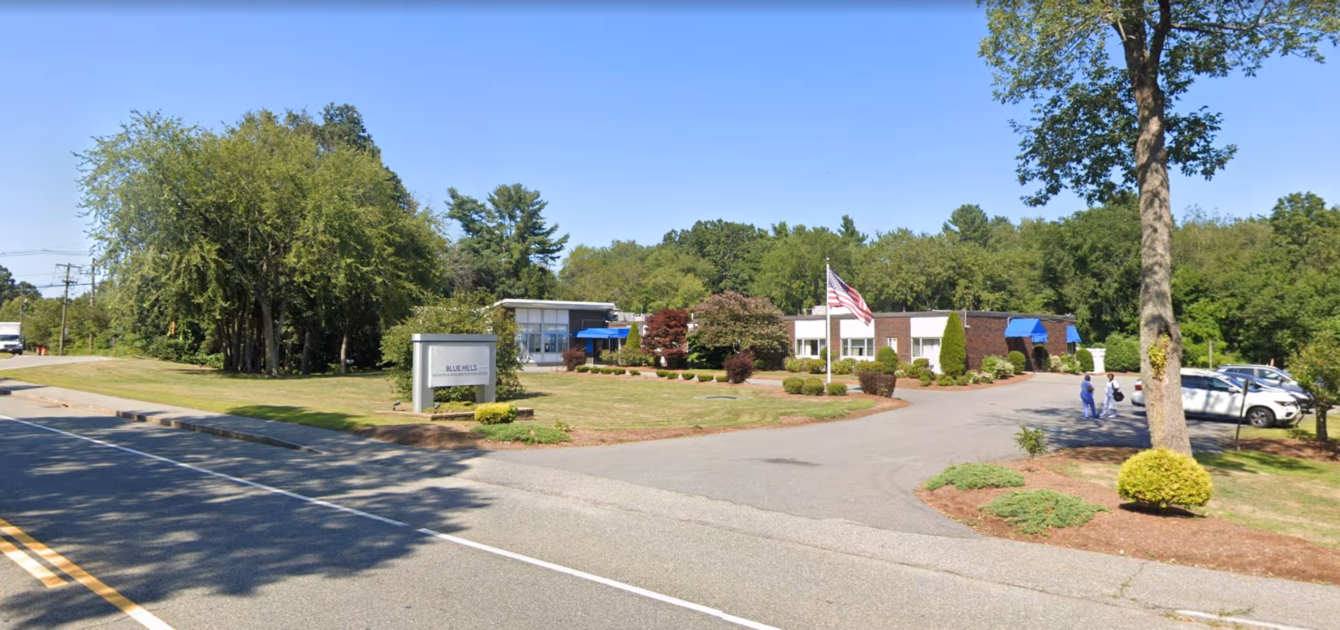 Exterior view of Blue Hills Health and Rehabilitation Center with sign, flag, and landscaping.