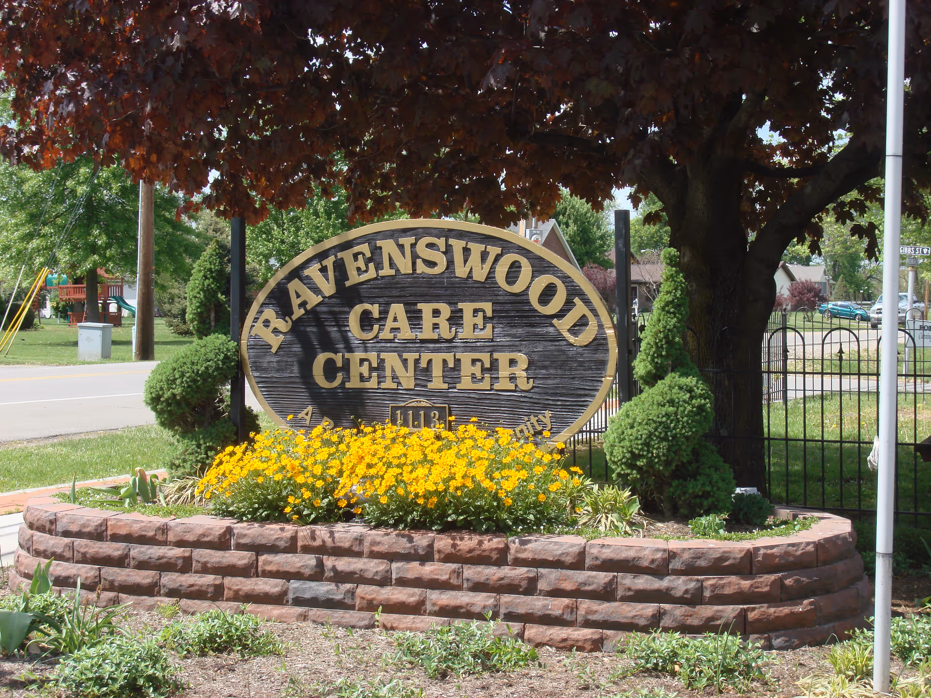 Exterior view of Ravenswood Care Center sign with flower beds and landscaping.