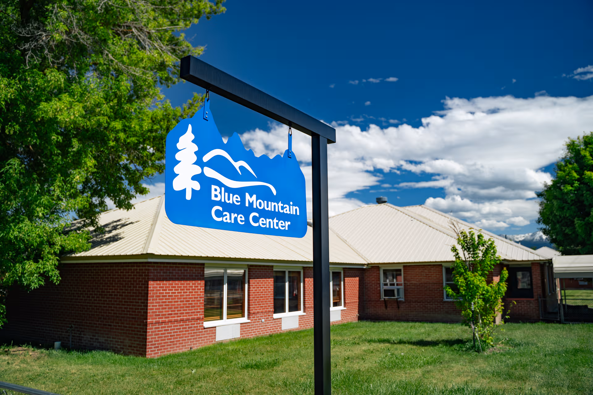 Blue Mountain Care Center sign outside a brick building with trees and blue sky.
