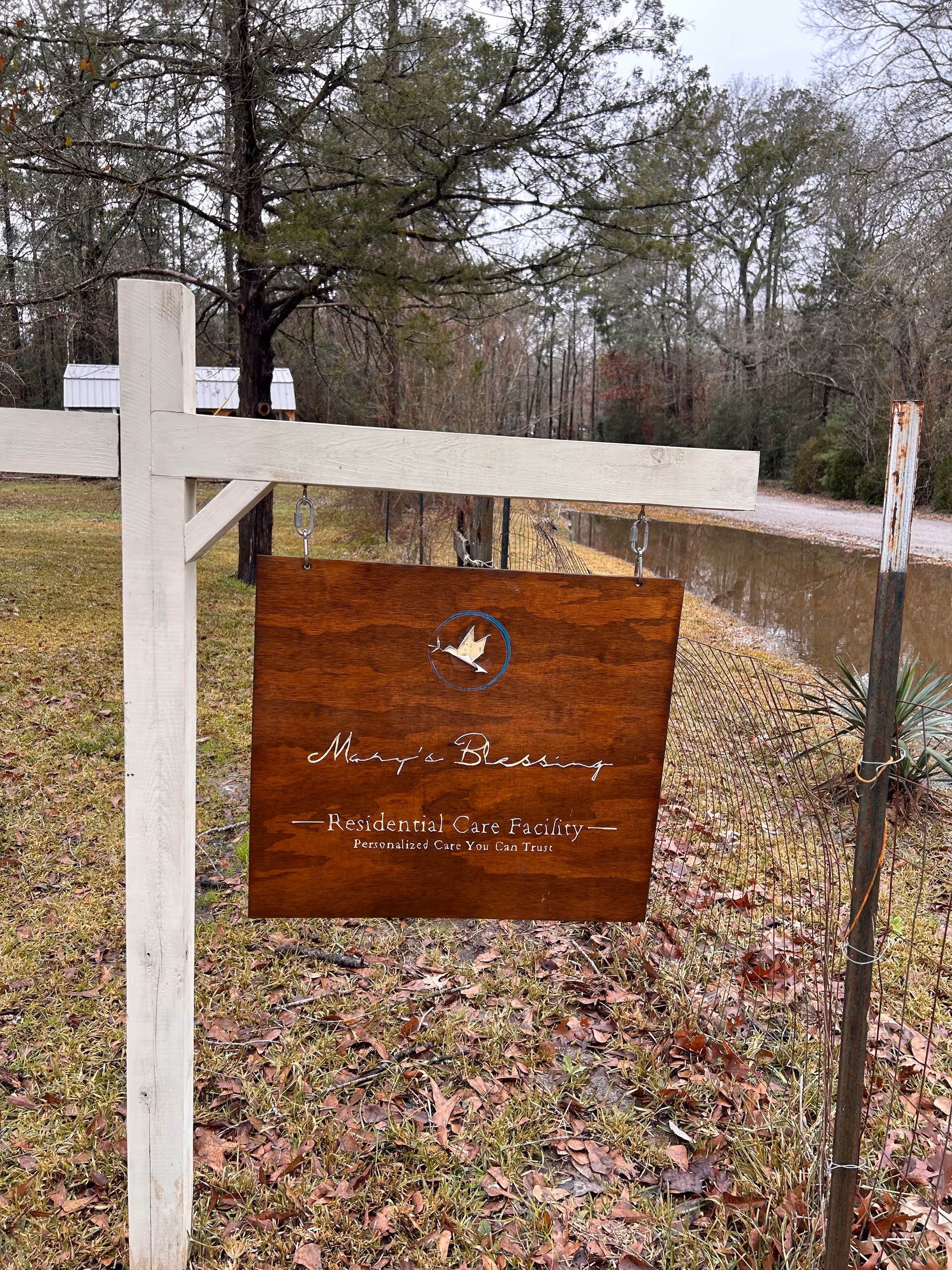 Wooden hanging sign reads 'Mary's Blessing Residential Care Facility' outdoors on a white post.
