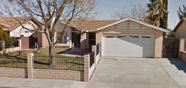 Exterior view of a single-story home with a two-car garage and fenced front yard.
