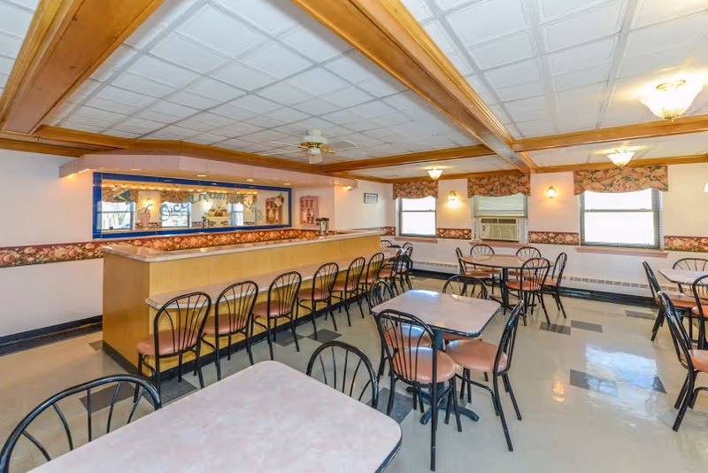 Bright dining room with multiple tables, chairs, and a long service counter.